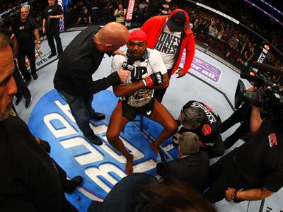NEWARK, NJ - APRIL 27:  Jon Jones (C) has his broken toe tended to while he is interviewed by Joe Rogan (R) after winning by knockout in round one against Chael Sonnen in their light heavyweight championship bout during the UFC 159 event at the Prudential